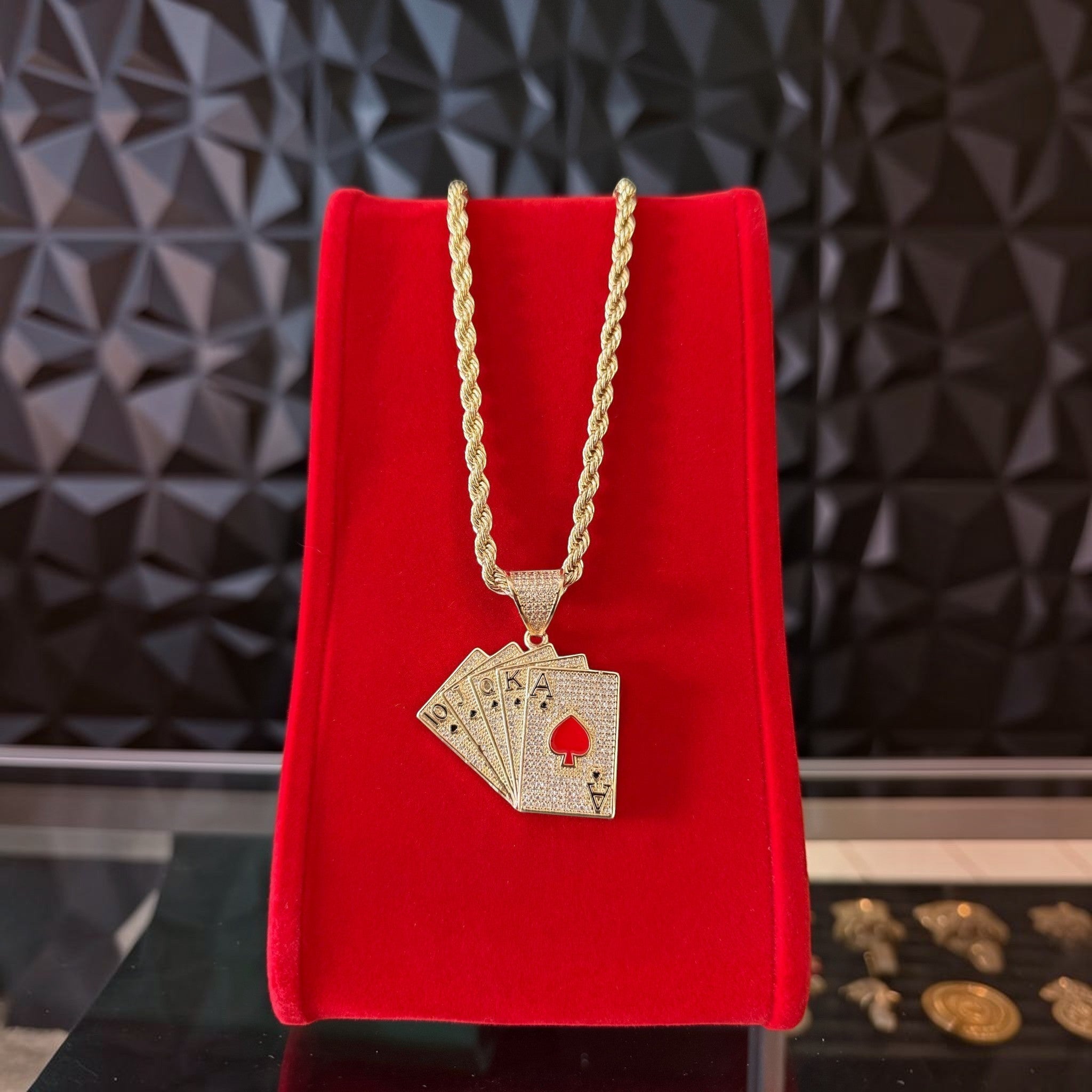 Kit de cadena torzal y dije de baraja con baño de oro 18k de El Rey Joyero sobre expositor de terciopelo rojo