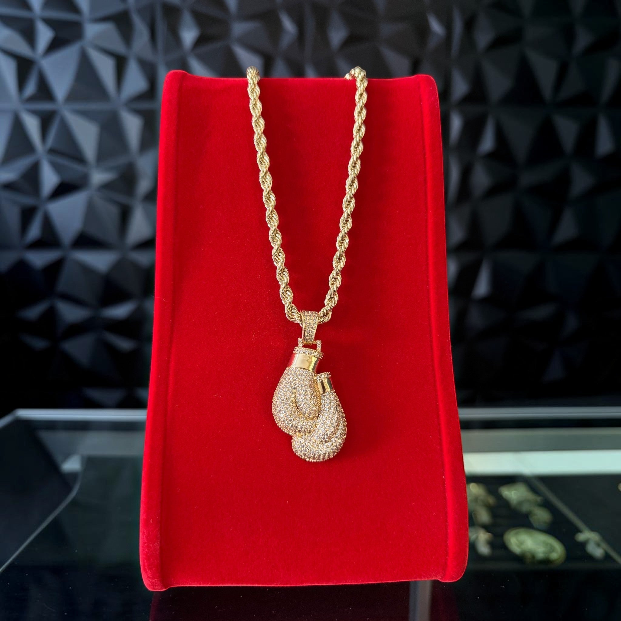 Cadena torzal con dije de guante de boxeo con cristales de El Rey Joyero en baño de oro 18k sobre exhibidor rojo